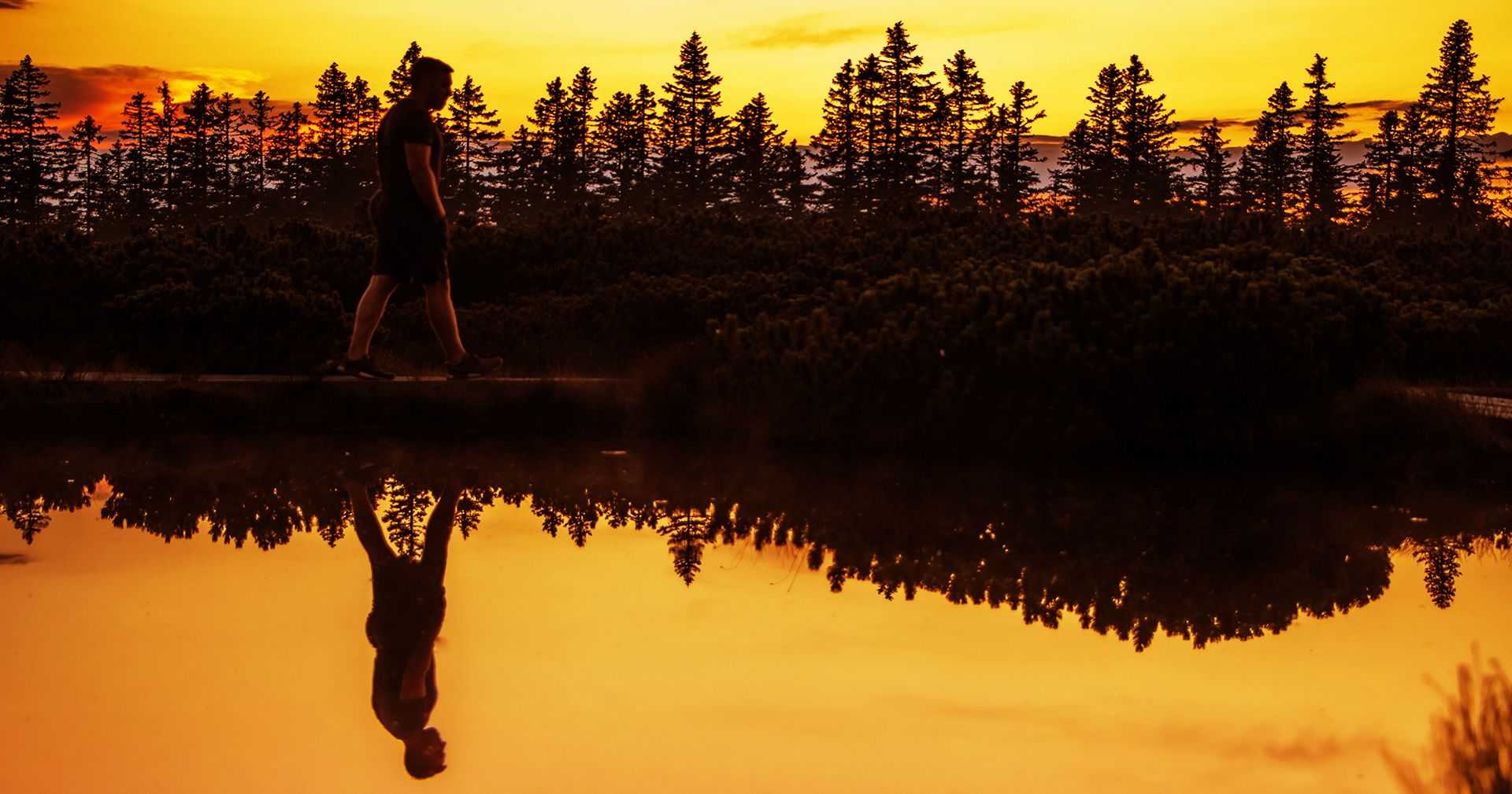 A man walking beside the lake during sunset